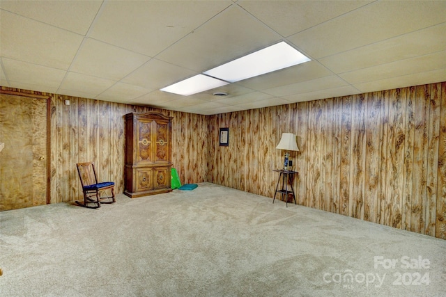 basement featuring wood walls, carpet, and a paneled ceiling