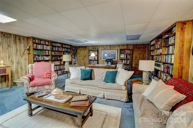 carpeted living room featuring a paneled ceiling and wood walls