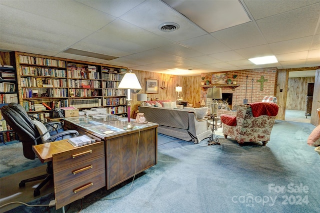 carpeted office featuring a fireplace, a paneled ceiling, and wood walls