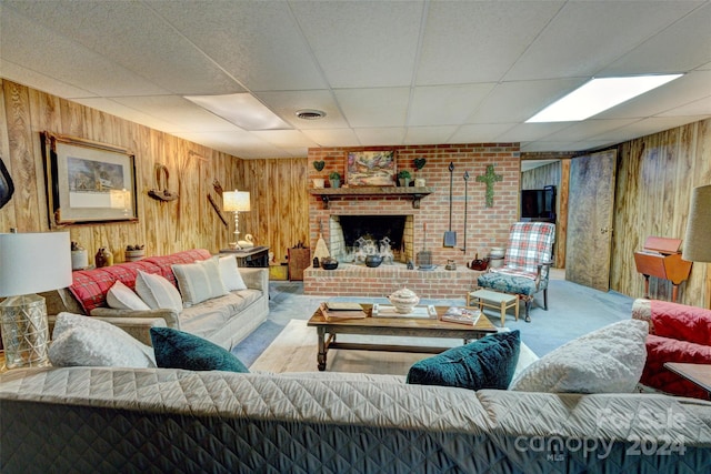 carpeted living room featuring wood walls, a fireplace, and a drop ceiling