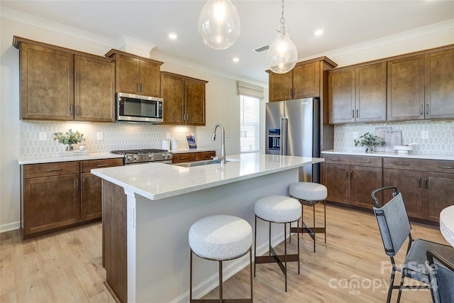 kitchen featuring high end appliances, light wood-type flooring, a kitchen island with sink, and hanging light fixtures