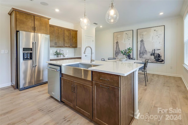 kitchen featuring stainless steel appliances, hanging light fixtures, a center island with sink, and light hardwood / wood-style flooring