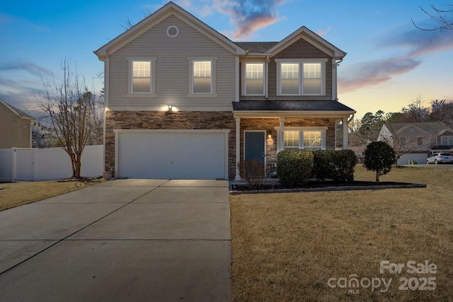 traditional-style house with concrete driveway, fence, a garage, stone siding, and a front lawn