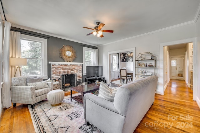 living room with plenty of natural light, crown molding, a brick fireplace, and light hardwood / wood-style flooring