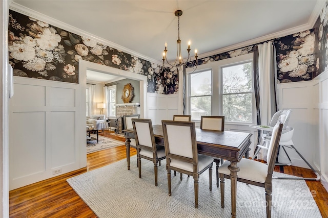 dining space with a chandelier, a decorative wall, wood finished floors, wallpapered walls, and crown molding