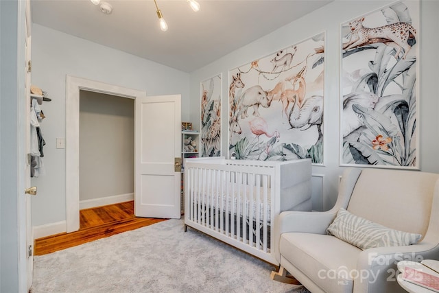 bedroom with lofted ceiling, a nursery area, baseboards, and wood finished floors