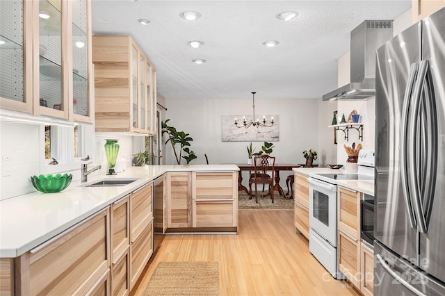 kitchen with light brown cabinetry, wall chimney range hood, pendant lighting, white range with electric cooktop, and stainless steel refrigerator