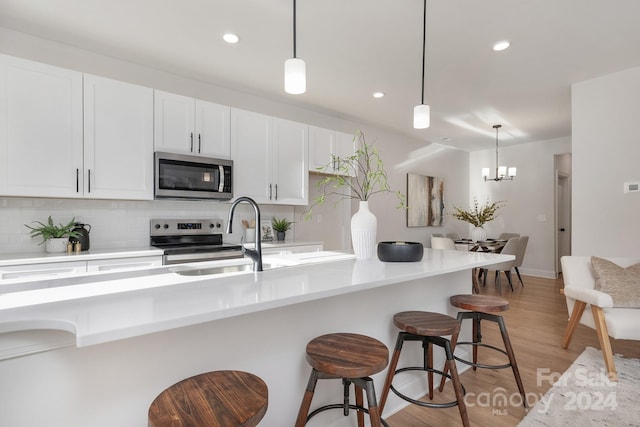 kitchen featuring white cabinetry, sink, hanging light fixtures, appliances with stainless steel finishes, and light wood-type flooring