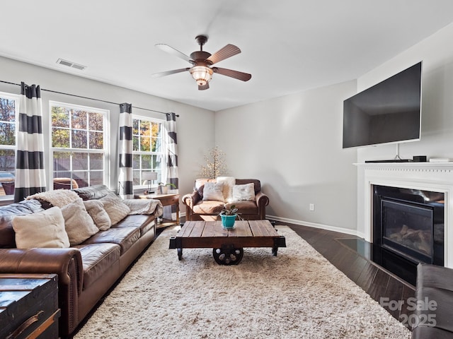 living area featuring visible vents, baseboards, a fireplace with flush hearth, ceiling fan, and dark wood-type flooring