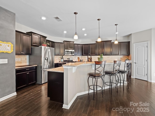 kitchen with light stone counters, dark wood-style floors, stainless steel appliances, visible vents, and dark brown cabinets