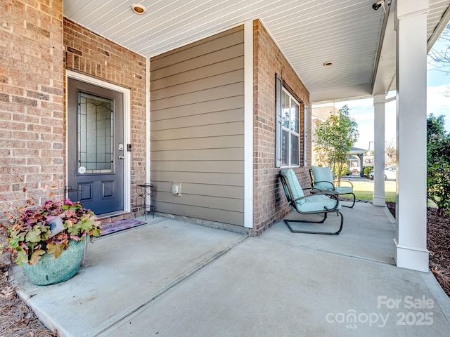 view of exterior entry featuring covered porch and brick siding