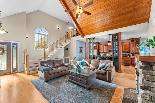 living room featuring light wood-type flooring, high vaulted ceiling, ceiling fan, and stairway