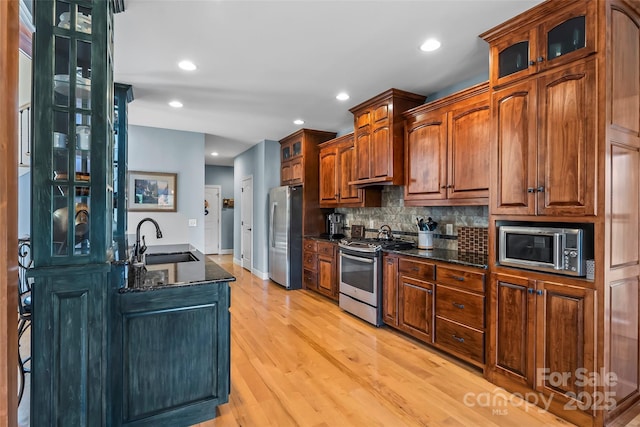 kitchen with stainless steel appliances, glass insert cabinets, a sink, and light wood finished floors