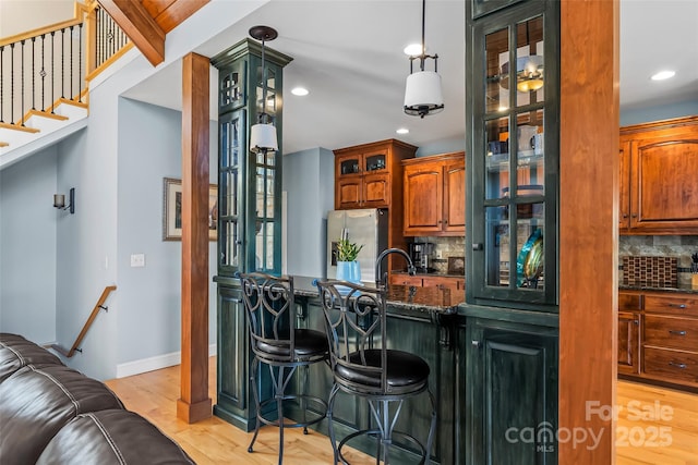 kitchen featuring decorative backsplash, stainless steel fridge with ice dispenser, light wood-style flooring, glass insert cabinets, and a kitchen bar