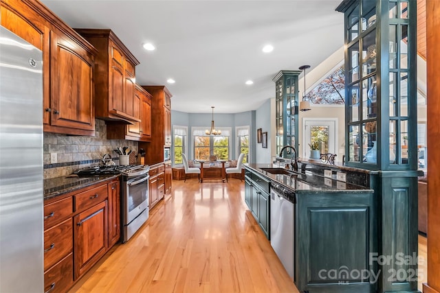 kitchen featuring a sink, appliances with stainless steel finishes, light wood finished floors, dark stone countertops, and tasteful backsplash