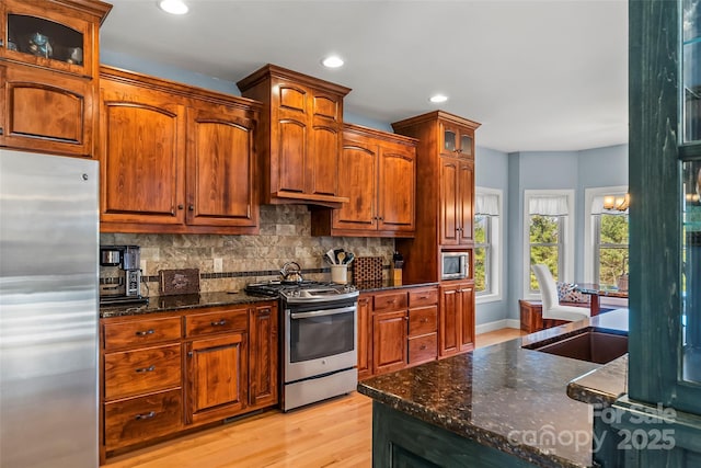 kitchen with recessed lighting, stainless steel appliances, light wood-style floors, tasteful backsplash, and glass insert cabinets