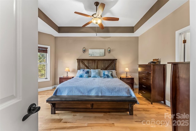 bedroom featuring light wood finished floors, baseboards, a tray ceiling, and a ceiling fan