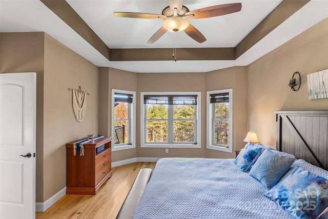 bedroom with a raised ceiling, light wood-style flooring, and baseboards