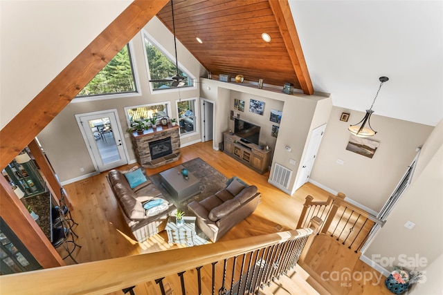 living area featuring high vaulted ceiling, a stone fireplace, baseboards, and wood finished floors