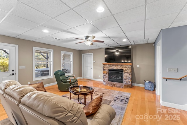 living room featuring light wood-type flooring, a healthy amount of sunlight, baseboards, and a stone fireplace