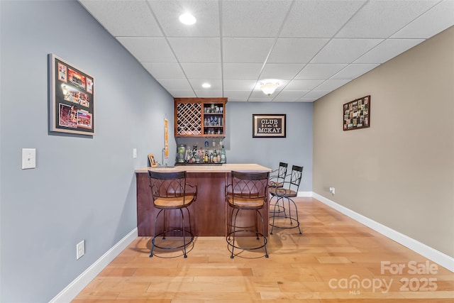 bar with recessed lighting, light wood-style floors, a bar, a drop ceiling, and baseboards