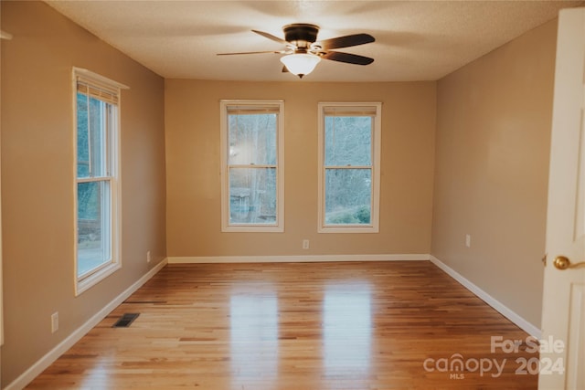 empty room with a textured ceiling, light hardwood / wood-style floors, a wealth of natural light, and ceiling fan