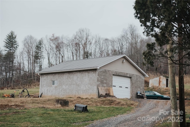 view of property exterior featuring stucco siding, driveway, metal roof, and an outbuilding