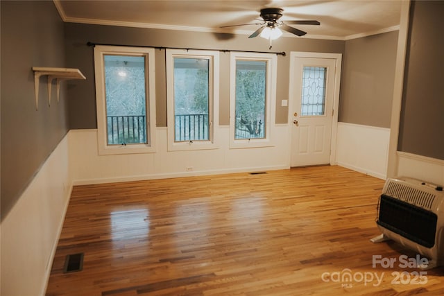 interior space with heating unit, a wainscoted wall, visible vents, and a ceiling fan