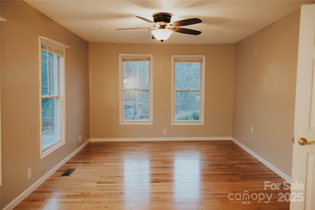 empty room with baseboards, visible vents, ceiling fan, and light wood-style floors