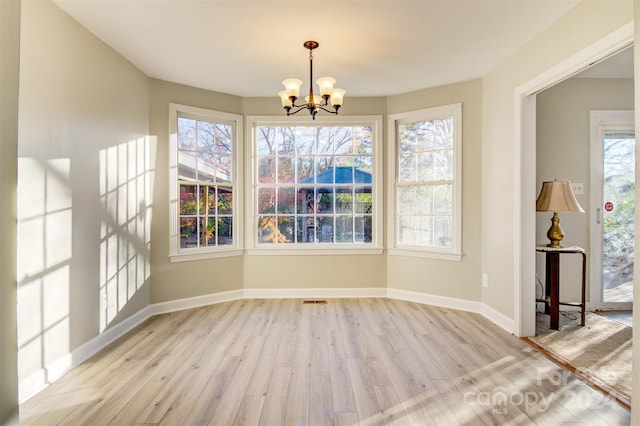 unfurnished dining area with a notable chandelier, plenty of natural light, and light hardwood / wood-style flooring