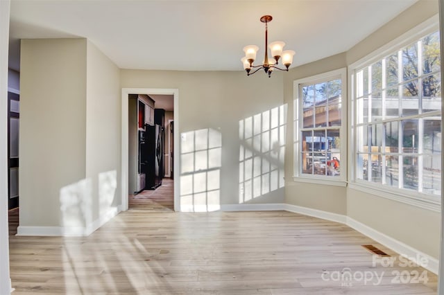 unfurnished dining area with light wood-type flooring and an inviting chandelier