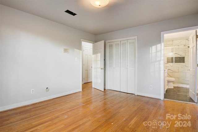 unfurnished bedroom with hardwood / wood-style floors, a closet, and ensuite bath