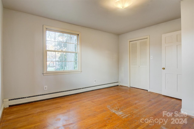 unfurnished bedroom featuring baseboard heating, a closet, and light hardwood / wood-style flooring