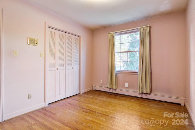 unfurnished bedroom featuring a closet, baseboard heating, and light hardwood / wood-style flooring