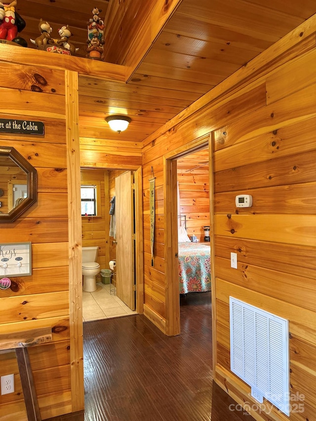 corridor with wood finished floors, wooden walls, wood ceiling, and visible vents