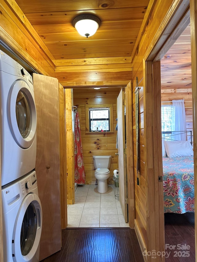 clothes washing area featuring wood finished floors, wood walls, wooden ceiling, stacked washer / dryer, and laundry area