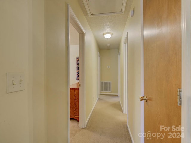 hall with light colored carpet and a textured ceiling