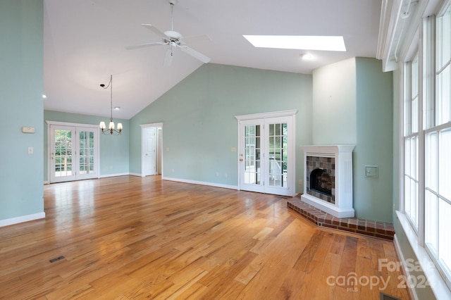 unfurnished living room with high vaulted ceiling, ceiling fan with notable chandelier, light hardwood / wood-style flooring, a skylight, and a tiled fireplace