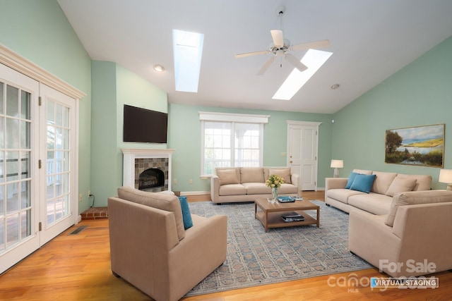 living room with a tile fireplace, light hardwood / wood-style flooring, vaulted ceiling, and ceiling fan