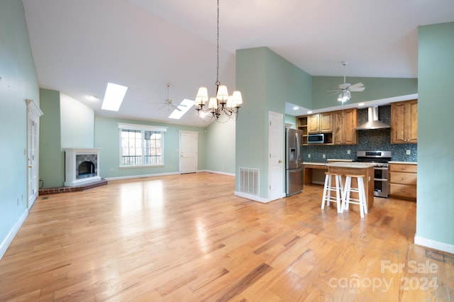 kitchen with a skylight, wall chimney range hood, light hardwood / wood-style floors, a breakfast bar area, and appliances with stainless steel finishes