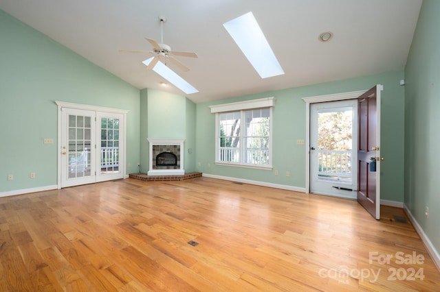 unfurnished living room featuring vaulted ceiling with skylight, ceiling fan, light hardwood / wood-style floors, and a fireplace