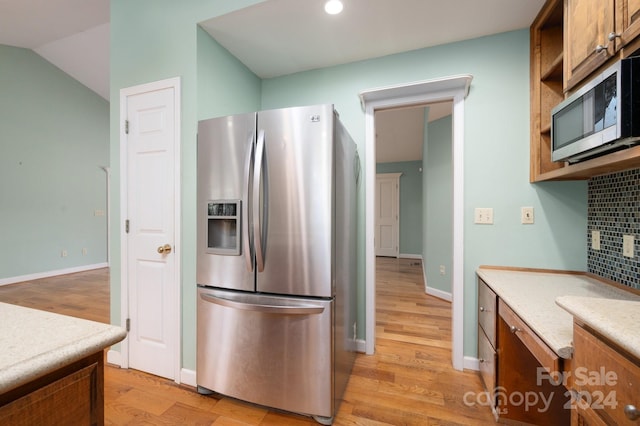 kitchen with tasteful backsplash, light wood-type flooring, lofted ceiling, and appliances with stainless steel finishes