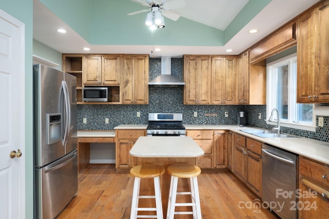 kitchen with sink, wall chimney range hood, lofted ceiling, a kitchen island, and appliances with stainless steel finishes