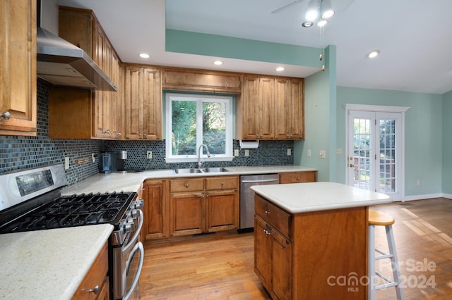 kitchen with appliances with stainless steel finishes, light wood-type flooring, wall chimney exhaust hood, sink, and a kitchen island