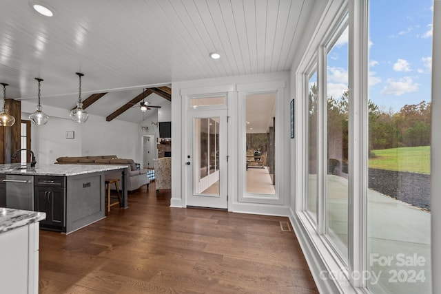 kitchen with lofted ceiling with beams, dark hardwood / wood-style flooring, pendant lighting, light stone countertops, and dishwasher