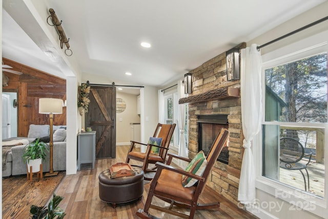 living area with a barn door, a stone fireplace, and hardwood / wood-style flooring