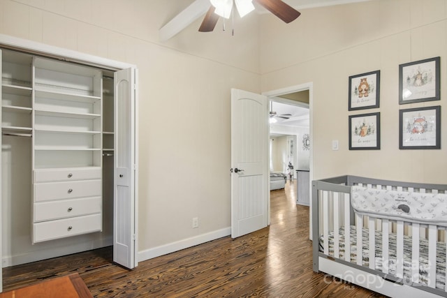 bedroom featuring dark hardwood / wood-style flooring, ceiling fan, beamed ceiling, a crib, and a closet