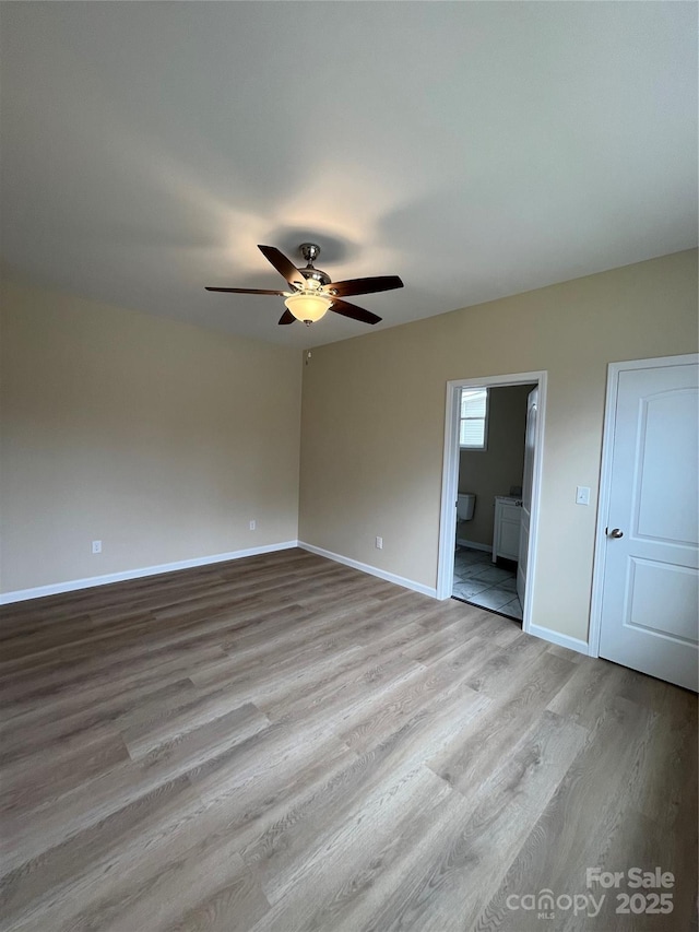 unfurnished bedroom with light wood-style floors, ceiling fan, baseboards, and connected bathroom