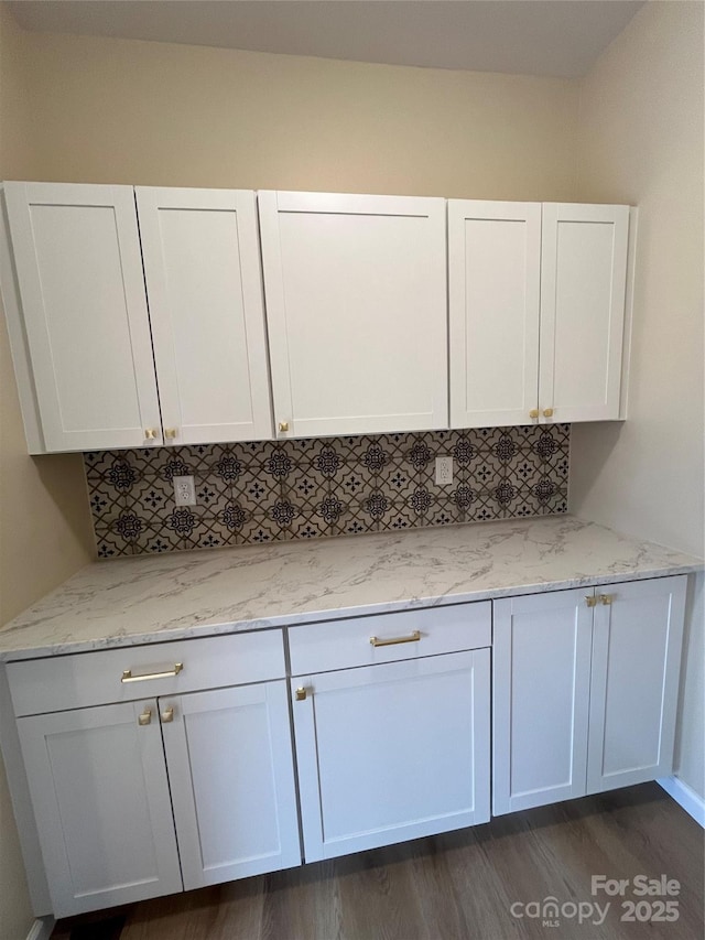 kitchen featuring light stone countertops, white cabinetry, dark wood-type flooring, and backsplash