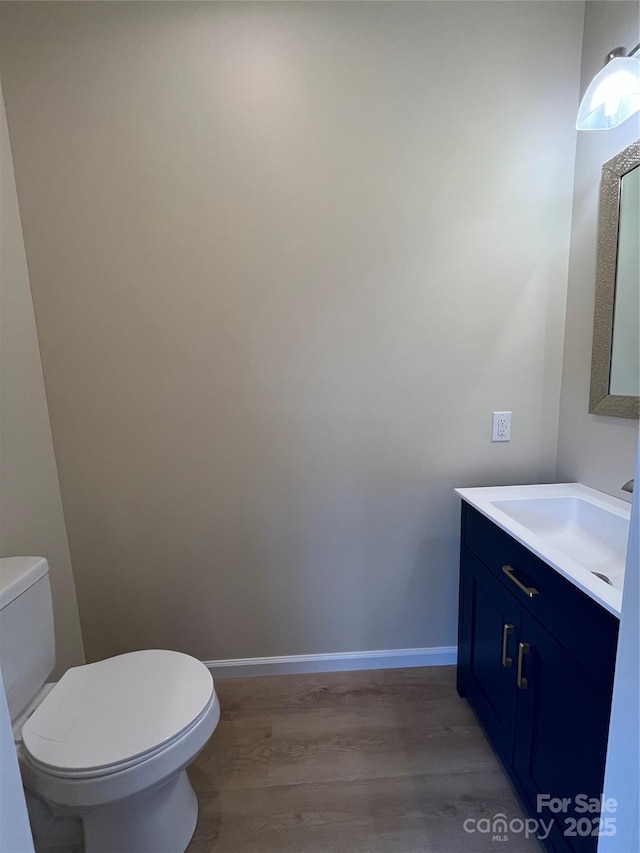 bathroom featuring toilet, baseboards, wood finished floors, and vanity